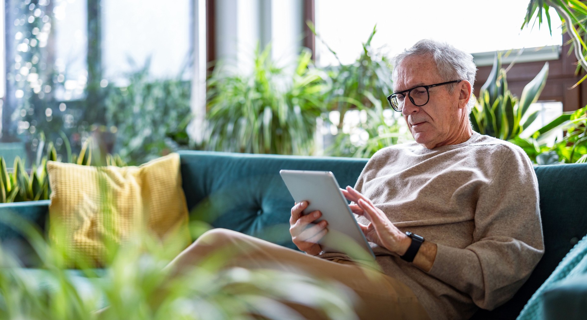 Cagary senior man using digital tablet while sitting on sofa in living room at home
