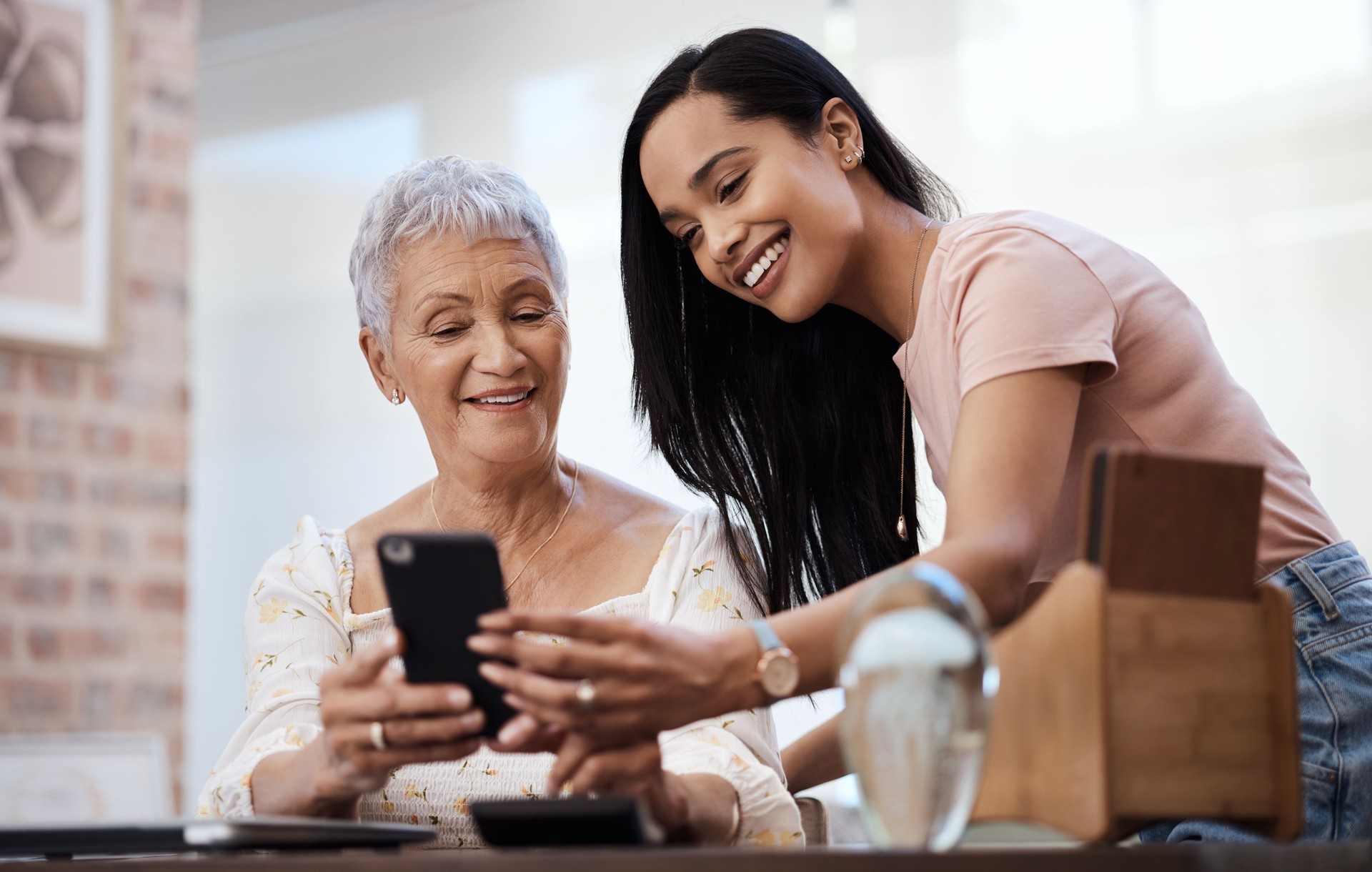 Shot of a young calgary woman using a smartphone with her elderly mother while going through finances at home