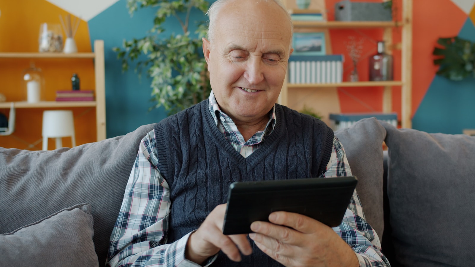 A senior man smiling warmly while confidently using a tablet at home